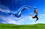 Beautiful athletic woman jumping on a green meadow with a scarf