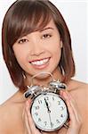 A naturally beautiful oriental woman make up free and holding an alarm clock just about to get to 12 o'clock