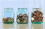 Saving money concept - coins in old jars on reflective surface against blue background