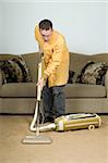 A young man vacuuming the carpet with an old vacuum cleaner