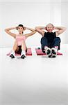 young woman and senior man doing abs in gym