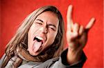 Closeup Portrait of Handsome Young Man with Long Hair Making Hand gesture and Sticking Out Tongue