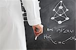 rear view of woman in lab clothes writing chemical formula on blackboard