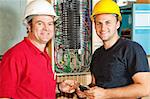Friendly master electrician and apprentice working on breaker panel.