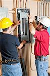 Two electricians repairing an electrical circuit breaker panel in an industrial setting.