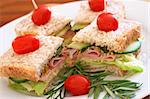 Tasty club sandwiches with green lettuce, grated cheese, smoked ham and wholegrain mustard on wholewheat bread with rosemary and tomatoes