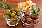 Two jars of green and black olives with stick of rosemary and croutons on wooden table background