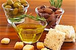 Two jars of green and black olives with stick of rosemary, croutons and slices of wholewheat bread on wooden table background