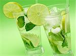 Two mojito cocktails with lime, mint leaves and ice on green background