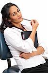 Beautiful brunette businesswoman wearing office clothes holding a diary and a pen relaxing on office chair. Isolated on white background with copy space