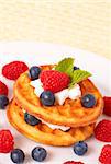 Small Belgian waffles with fresh raspberries, blueberries, mint leaves and cream on white plate