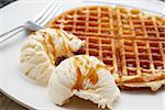 Freshly baked waffle with two scoops of vanilla ice-cream covered with syrup, served on a white plate