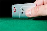 Hand holding a pair of aces on green gaming table - focus on cards and hand