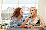 Two girls in cafe confidentially look against each other and smile