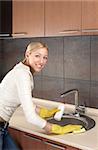 The smiling blonde washes ware in a bowl on kitchen