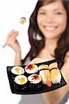 Smiling young woman presenting a plate of sushi. Shallow depth of field, focus on sushi.