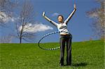 Beautiful young woman doing hula hoop outdoors on a sunny spring day.