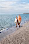 Financially secure retired senior couple enjoys a walk on a beautiful beach.  Wide angle view with room for text.