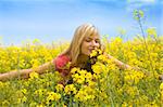 happy blond girl with open arms smelling some flowers in a yellow field