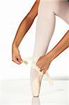 Young female ballet dancer showing how to tie a ballet Pointe Shoe against a white background. NOT ISOLATED