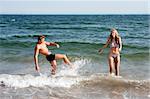 Beautiful young couple playing in the ocean splashing water, heaving fun on a summer day