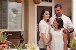 Small Hispanic Mother, Father and Daughter in Front of Their Home.