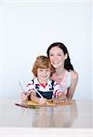 Mother and son writing at home and smiling to the camera