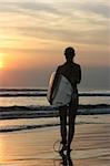 Silhouette of a girl with surf in front of the ocean at dawn