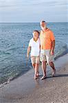 Happy senior couple take a stroll on a beautiful tropical beach.