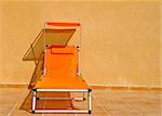 A vivid orange sun lounger on a tiled floor against a buff concrete wall