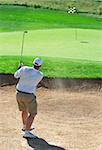 Young male golfer hitting the ball from the sand bunker on a beautiful summer day