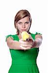 Pretty girl in a green dress is holding a banana as a gun, isolated on white