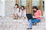 Mother using Laptop and Daughters using Handheld Video Games