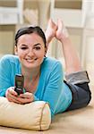 Attractive brunette woman lying on floor with cell phone and smiling at camera. Vertical