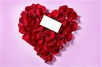 Red rose petals in heart shape with a copy space blank note