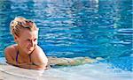 Beautiful blonde happy girl in hotel swimming pool with flower in long hair