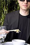 Man in a black suit is eating asian food with chop sticks