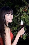 Latina woman outside with green plants in the background with a red drink and a red drink