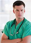An attractive young doctor posing. He is looking directly at the camera.  Vertically framed shot.