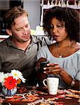 Caucasian man and African American woman in coffee house with cell phone