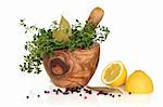 Herb leaf selection of  thyme and bay in an olive wood mortar with pestle with peppercorns and lemon halves.