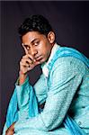 Beautiful face of an Indian Hindu young man with earring wearing blue Dhoti. Portrait of handsome Desi male sitting and thinking, isolated.