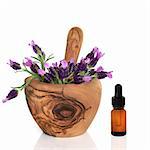 Lavender herb flowers in an olive wood mortar with pestle, with an aromatherapy essential oil glass dropper bottle, over white background.