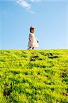 Little girl on green grass hill over blue sky