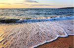 Sea surf wave break on sunset sandy coastline