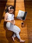 Top view of a young pregnant woman lying on the floor with a laptop computer and a cup of tea.