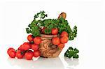 Tomatoes on the vine and parsley herb leaf sprigs in an olive wood mortar with pestle, over white background.