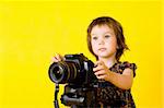 Portrait of baby girl holding photo camera isolated on yellow background