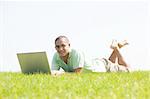 A young men lying on the grass in the park using a laptop