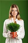 Portrait of a beautiful young woman holding a plant on her hands, isolated on a green background